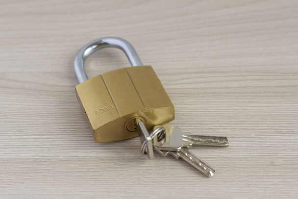 Closed padlock with keys in the keyhole on a light wooden background. - Photo, Image