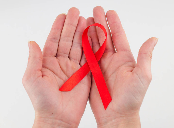 медицинская концепция и медицина - женские руки с красной лентой информированности о СПИДе. - Фото, изображение