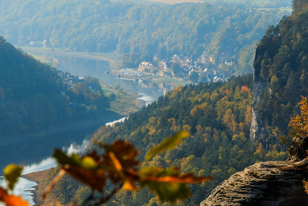 ザクセン・スイスのエルベ渓谷の眺め。秋の日差しと木の川のコース。ドイツのエルベ砂岩山脈にある岩と建物 - 写真・画像