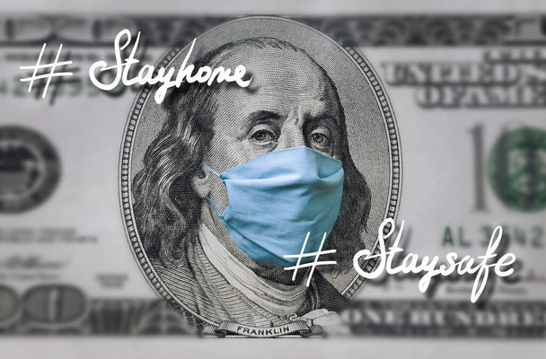Blue medical mask on the face of Benjamin Franklin with a hundred dollar bill. Inscription with hashtag: # Stay home, stay safe. Concept of global economic crisis, coronavirus, quarantine COVID-19. - Fotografie, Obrázek