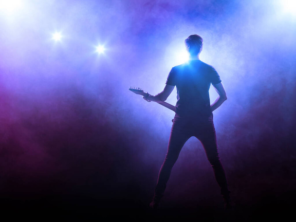 Силуэт гитариста, выступающего на сцене перед зрителями
.   - Фото, изображение