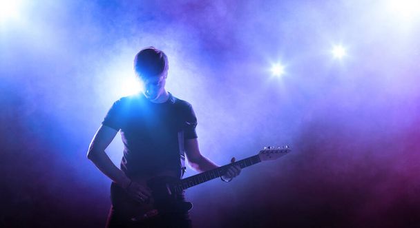 ステージ上のギタープレーヤーのシルエットを煙とスポットライトで青の背景に - 写真・画像