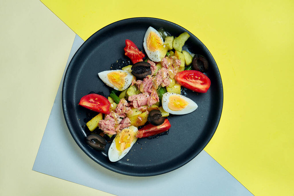 Tasty Nicoise Salad served in black plate on colored background. Close up view on salad with tomato, eggs, tomatoes, potato and tuna - Fotoğraf, Görsel