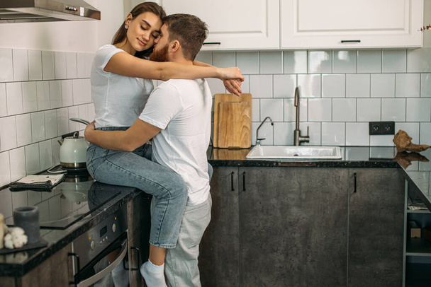 beautiful married couple kissing in kitchen at home - Фото, изображение