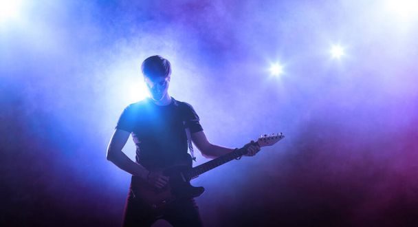 silueta kytaristy na jevišti na modrém pozadí s kouřem a reflektorem - Fotografie, Obrázek