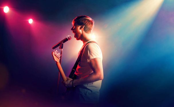 Gitar çalıp mikrofonla şarkı söyleyen bir müzisyen. Sahnede müzikal performans - Fotoğraf, Görsel
