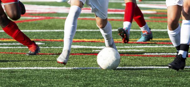 Beine von High-School-Fußballern, die den Ball während eines Spiels auf einem Rasenplatz kontrollieren und jagen. - Foto, Bild