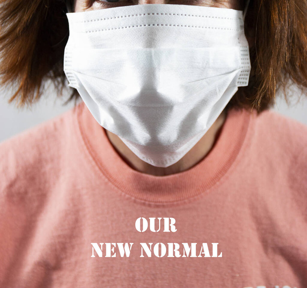 Maschera viso che copre il viso su una donna whos camicia legge il nostro nuovo normale a causa del coronavirus COVID-19
. - Foto, immagini