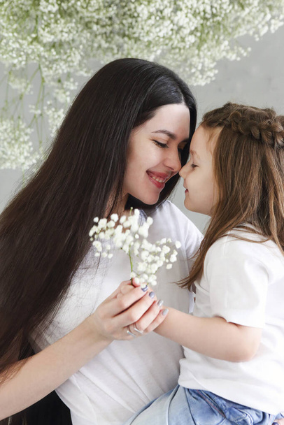 Young brunette mother and little daughter stand near the wall with big flowers wreath. Mother's day concep - Photo, Image