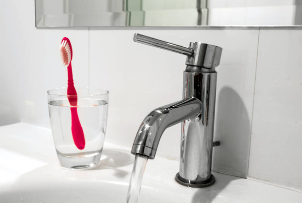 Bílá koupelna kohoutek a umyvadlo s vodou sklo a zubní kartáček - Fotografie, Obrázek