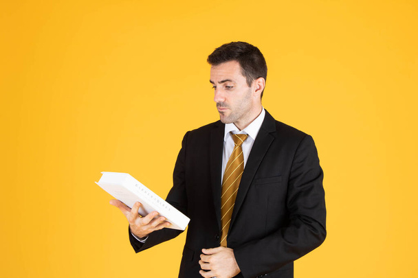 Retrato de un hombre de negocios guapo con traje blanco y corbata mientras sostiene un libro con fondo amarillo
. - Foto, Imagen