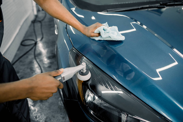 Detailing and polishing of car headlight on car. Hands of dark skinned worker with orbital polisher in auto service polishing car lights - Photo, Image