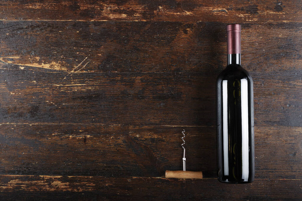 closed wine bottle and corkscrew on a brown wooden background. place for text. bottle without labe - Foto, Bild