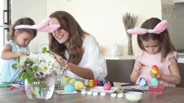 Χαρούμενη οικογένεια που ετοιμάζεται για το Πάσχα. μητέρα με κόρες με αστεία αυτιά κουνελιού που βάφουν μαζί πασχαλινά αυγά, 4K. - Πλάνα, βίντεο