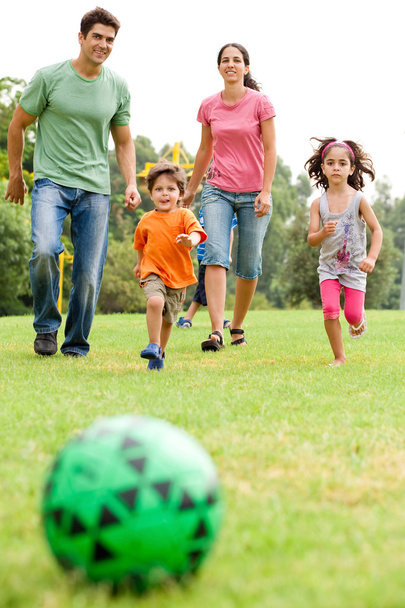 Perhe pelaa jalkapalloa puistossa
 - Valokuva, kuva