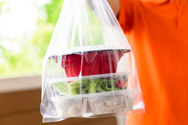 Cajas de comida asiática en bolsas de plástico entregadas al cliente en casa por el repartidor hombre en uniforme naranja
 - Foto, imagen