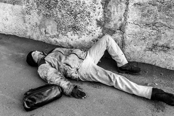 Бездомна брудна жінка лежить під стіною і спить на землі. Жіноча сумка неподалік
 - Фото, зображення