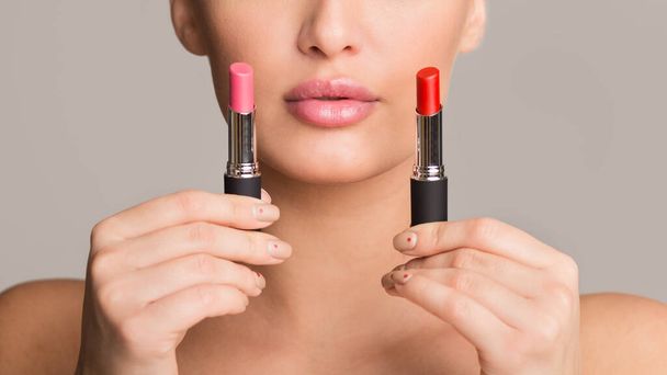 Difficult choice. Girl holding two lipsticks, gray background - Фото, изображение