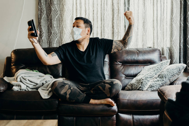 Asian bearded man sit on couch in living room at home. Looking at cell phone. - Zdjęcie, obraz