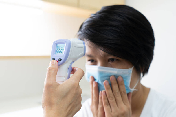 A nurse using a digital thermometer to measure temperature of a woman patient that gets sick. covid-19, coronavirus, medical, healthcare, fever concept - Photo, image