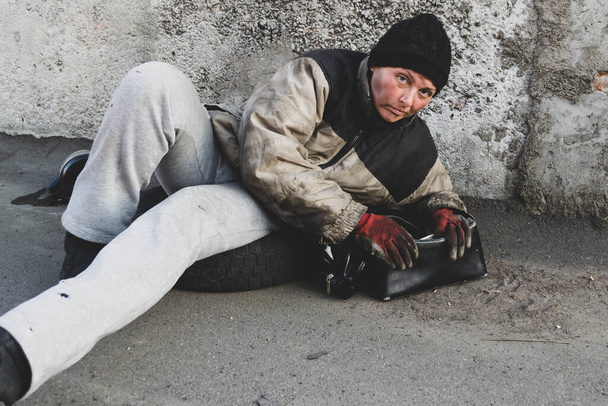 Бездомная грязная женщина лежит на земле и держит сумочку
 - Фото, изображение