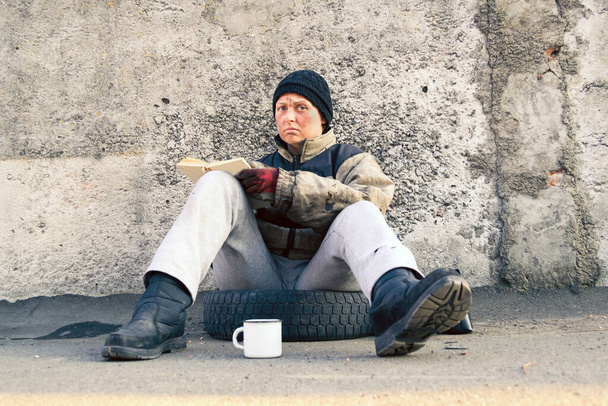 Špinavá bezdomovkyně sedící a prosící o pomoc a čtoucí knihu - Fotografie, Obrázek