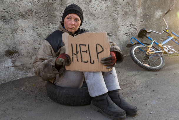 Бездомная грязная женщина сидит и просит прохожих о помощи.
 - Фото, изображение