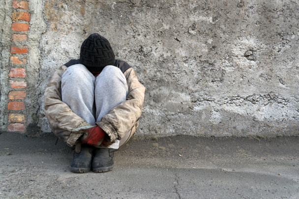 Sale sans-abri femme assise sous un mur gris étreignant ses jambes
 - Photo, image