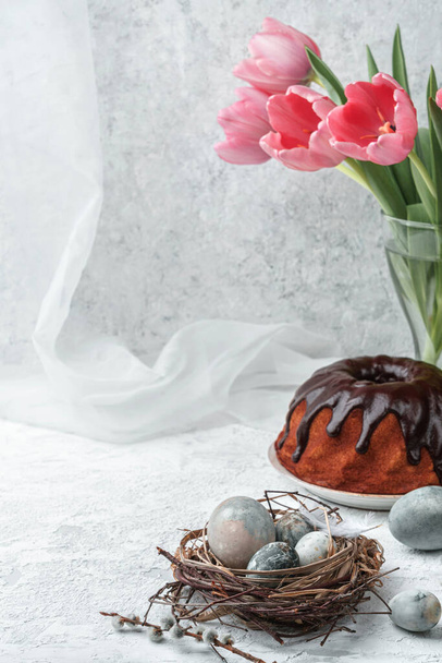 イースターの卵、巣、春のチューリップの花と白い背景にチョコレートとイースターケーキ。ハッピーイースターの休日 - 写真・画像