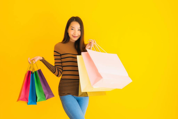 Portrait belle jeune femme asiatique sourire heureux avec beaucoup de couleur sac à provisions de grand magasin sur fond jaune isolé
 - Photo, image