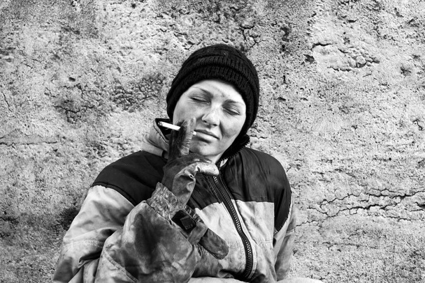 Mocskos hajléktalan nő ül egy cigarettával a kezében. - Fotó, kép