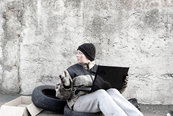 Mujer sucia sin hogar sentada con portátil en su regazo
 - Foto, Imagen