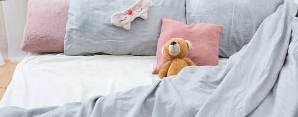bed with teddy bear on gray linens - Fotó, kép