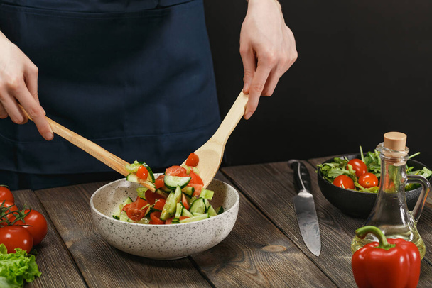 Woman mixing fresh healthy vegetable salad on wooden table. Female hands with copyspace. - Foto, Bild