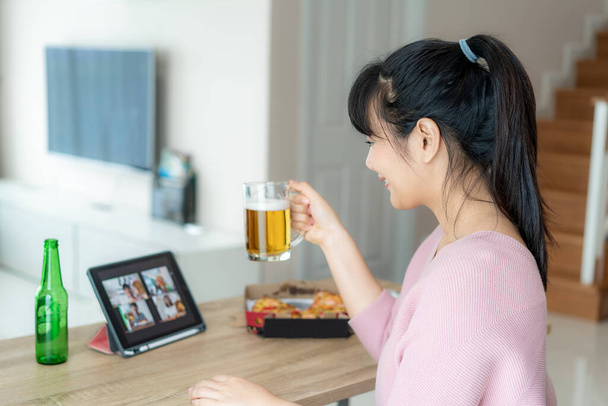 Asian woman virtual happy hour meeting party and drinking alcohol beer online together with her friend in video conference with digital tablet for a online meeting in video call for social distancing for infection risk. - Photo, Image