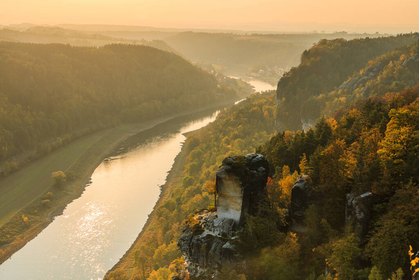Flusslauf der Elbe in der Sächsischen Schweiz im Herbst. Felsen mit Steinen und Wälder im Sonnenschein. Sonnenuntergang am Horizont über dem Elbtal. Bäume in saisonalen Farben - Foto, Bild
