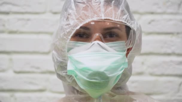 Young girl in protective suit, respirator, glasses and medical mask on her face shakes head left and right and say not. Woman nods her head up and down and say yes on white brick wall background. - Imágenes, Vídeo