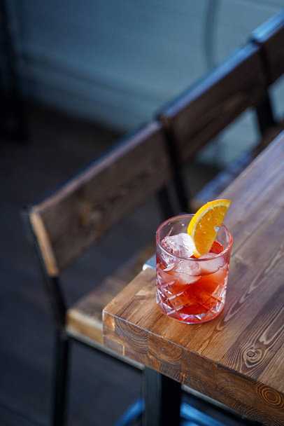 Negroni with a slice of orange on wooden table in a bar, cold colours, cold light, modern bar - Foto, afbeelding
