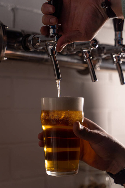Mężczyzna wlewający jasnozłote piwo do szklanki z kranu, zalać białą pianką, zamknąć ręce - Zdjęcie, obraz