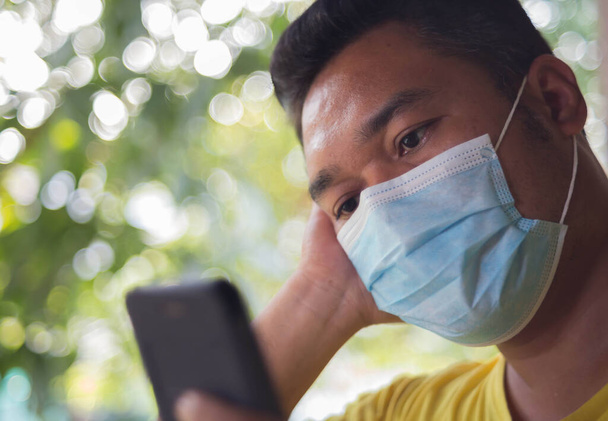 A man wearing a surgical face mask works over the phone at home. - Photo, Image