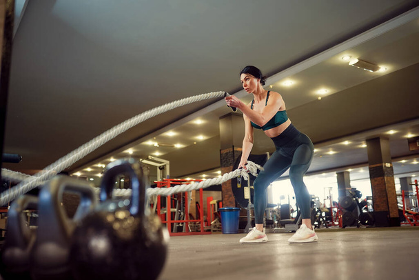 Кавказька жінка, одягнена в спортивний одяг, проводить тренування з бойовими мотузками в спортзалі - Фото, зображення