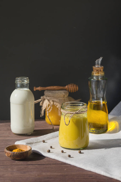 Turmeric-based golden milk healing drink and ingredients on black background. Prevention of diseases and strengthening immunity. - Photo, Image