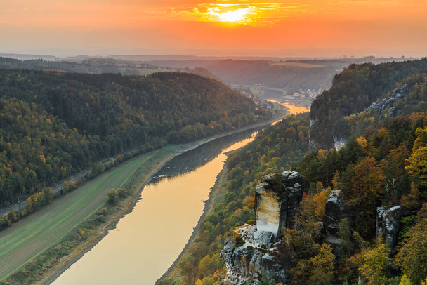 Landscape with the Elbe valley in the evening. Saxon Switzerland National Park with a view from the Bastei Bridge with the Elbe and rocks, trees and forests in the autumn mood with an orange horizon - Foto, afbeelding