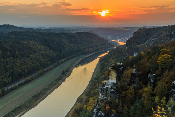 Pohled na krajinu národního parku Saské Švýcarsko s údolím Labe ve večerních hodinách. Pohled z mostu Bastei na skály, stromy a lesy s oranžovým západem slunce - Fotografie, Obrázek