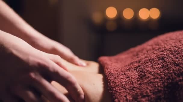 Detailní záběr Mladý masér provádí masáž zad ženě s tetováním v masážní místnosti s tlumeným světlem na pozadí svíček. Koncept nízkoklíčové prémie masáže - Záběry, video