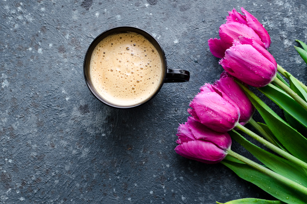 Cup of coffee with foam and bouquet of pink tulips on black background. Breakfast on Mothers day, Valentines Day or Womens day. Romantic morning concept. Top view. Copy space. - Foto, imagen