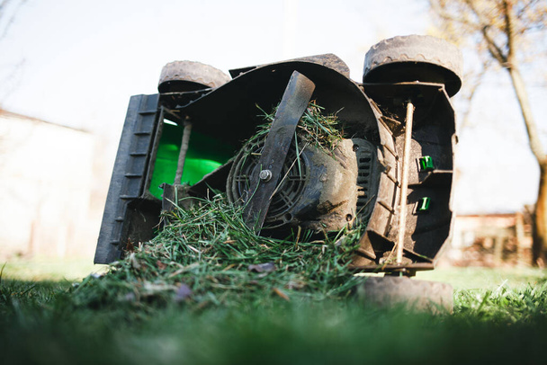 Газонокосилка, переполненная травой, лежит на боку
 - Фото, изображение