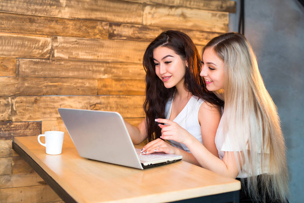 two beautiful young women are sitting at a table with a laptop - Φωτογραφία, εικόνα