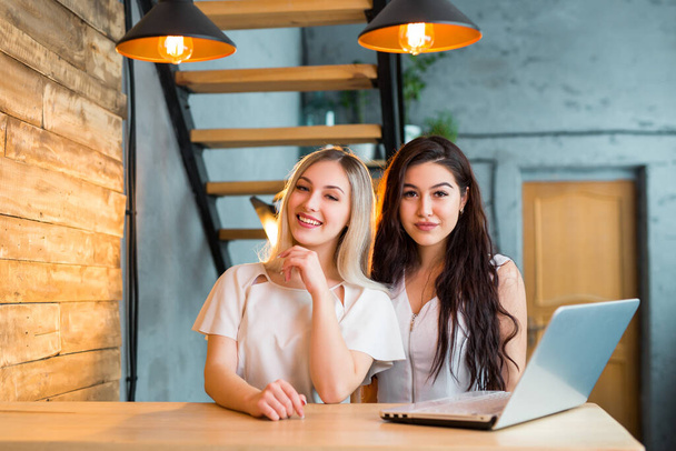 two beautiful young women are sitting at a table with a laptop - Photo, image