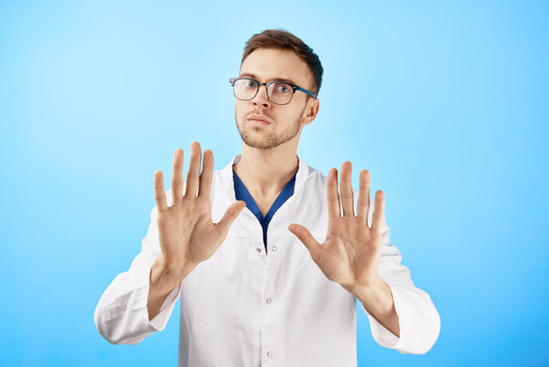 Serious doctor shows a gesture with his hands to the camera, stop panic, keep calm concept isolated on blue background - Zdjęcie, obraz